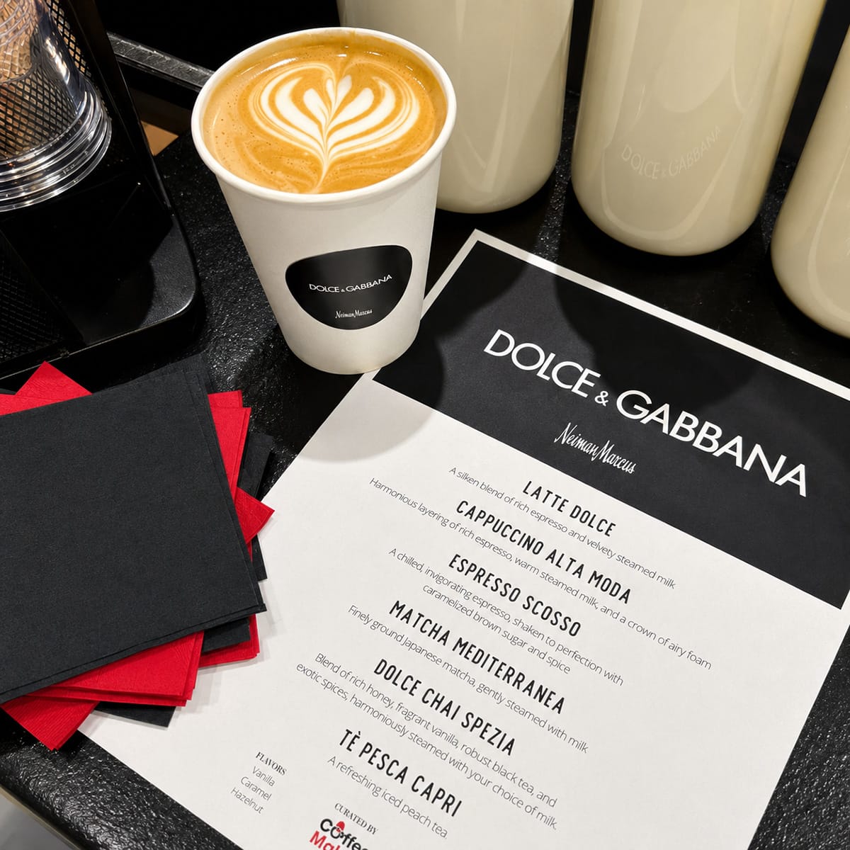 Latte with a Dolce & Gabbana-branded cup, custom drink menu, and coordinated black-and-red napkins prepared by Coffee Malem.